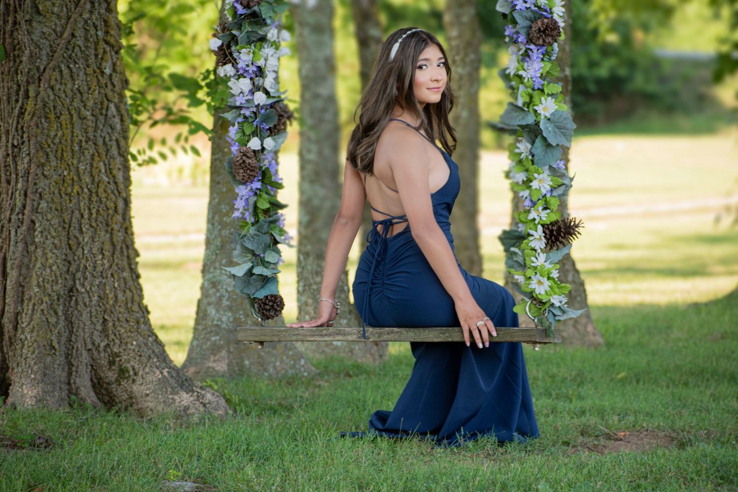 Garden portrait with blue dress between trees adorned with floral decorations.