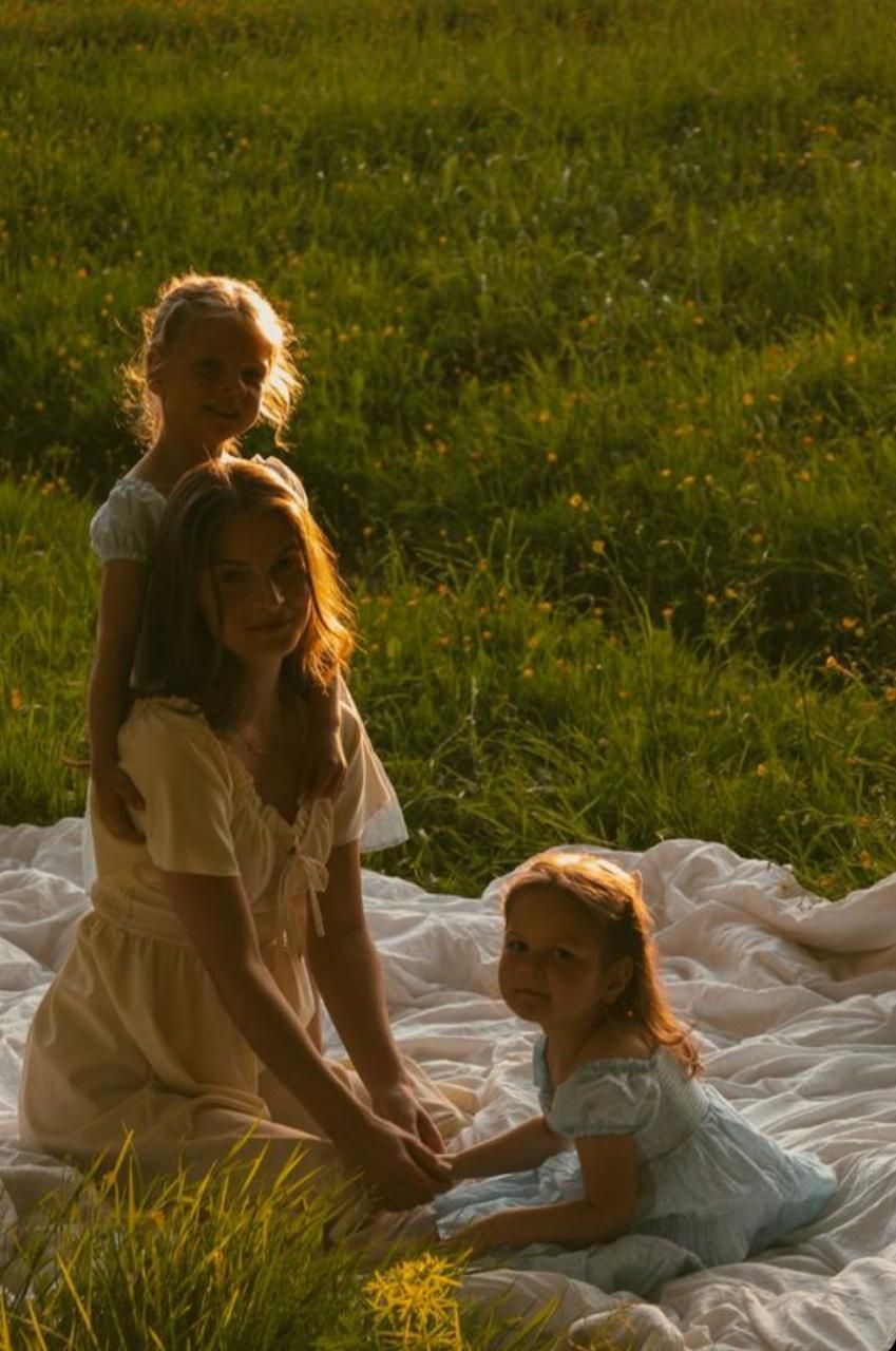 People relaxing on white blanket in sunlit grassy meadow during golden hour.