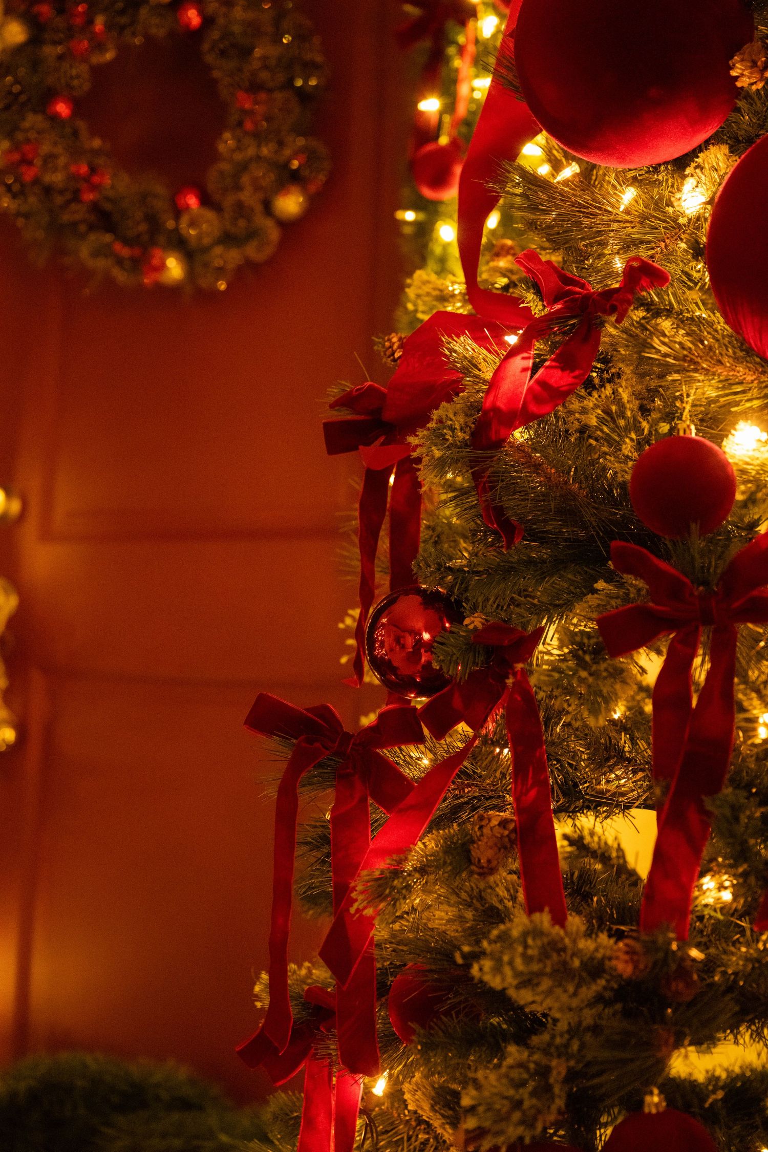 Close-up of Christmas tree decorated with red bows and ornaments glowing with warm holiday lights.