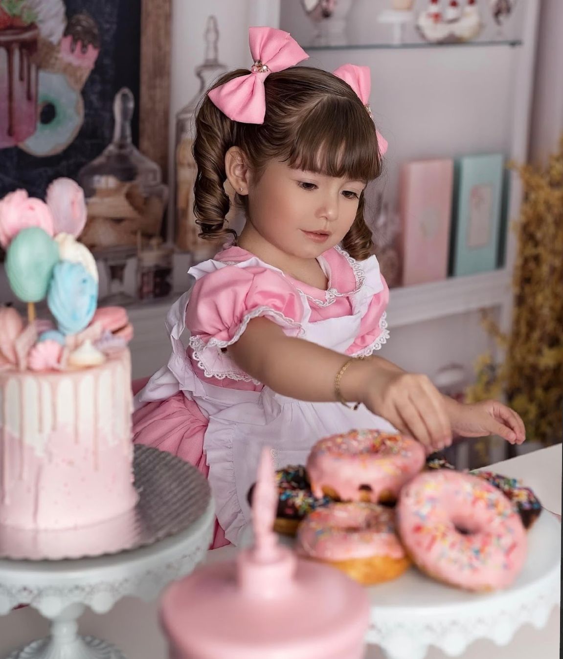 A pink and white party scene with donuts and cake on display at a pastel-colored dessert table.