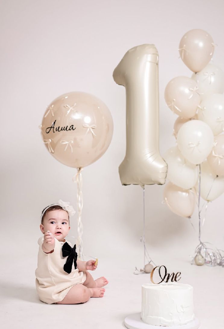 A series of minimalist first birthday photos with white and cream balloons against a light backdrop.