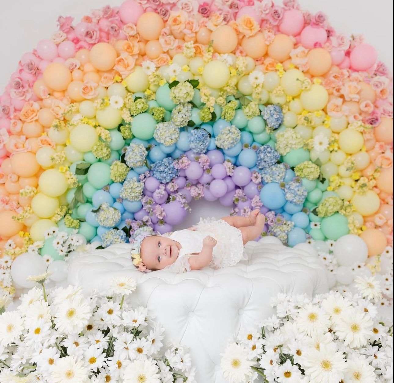 Colorful balloon arch installation in pastel rainbow colors against a white background with black splatters.