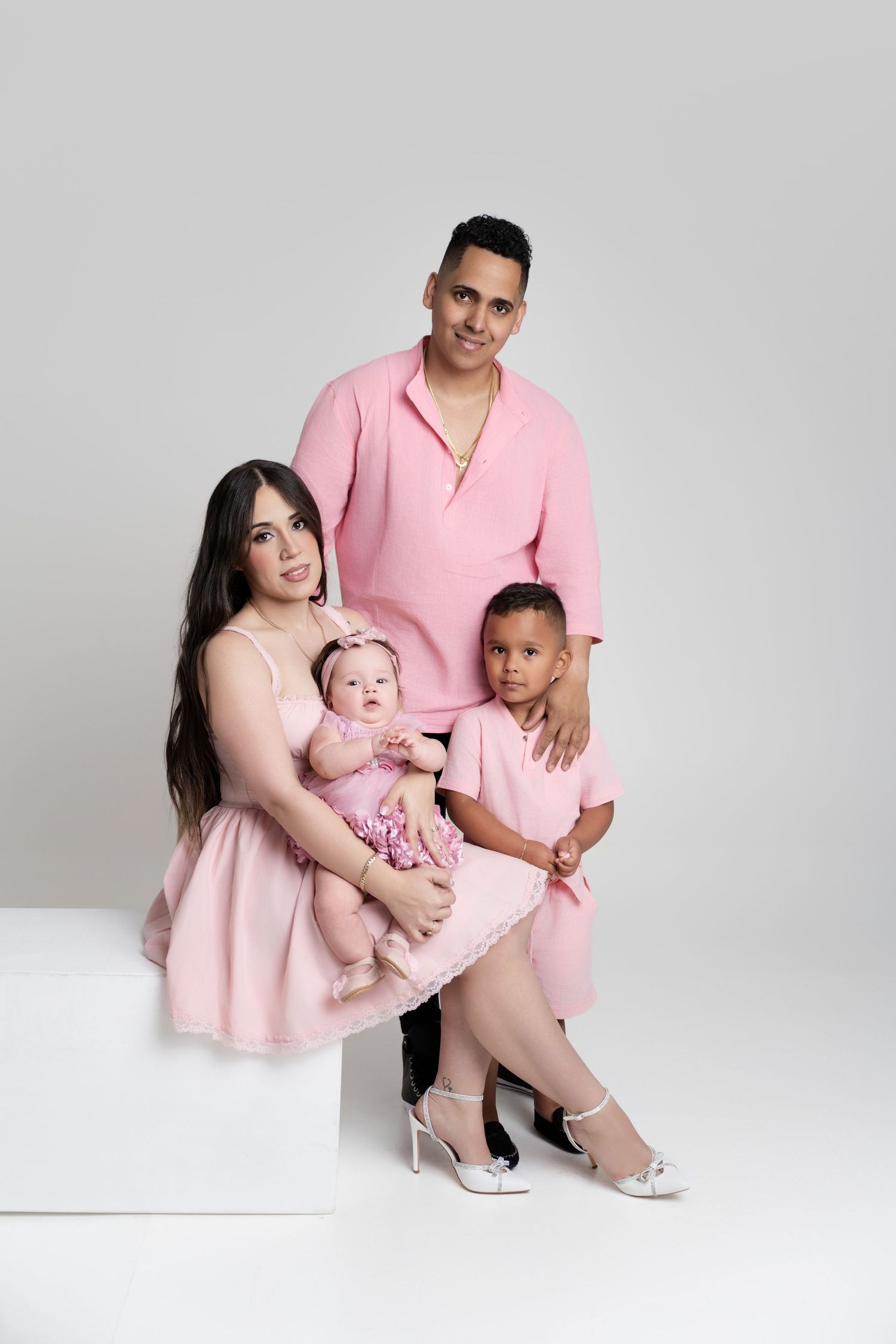 Family of four posing in matching pink outfits, mother holding baby girl, father standing behind with young child.