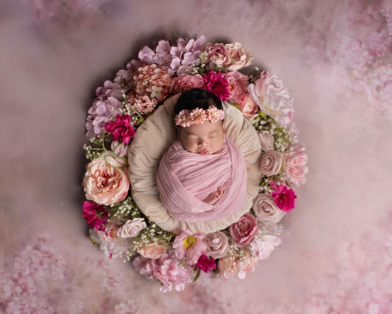 Newborn baby wrapped in pink swaddled in a floral wreath with roses for a professional newborn photo.