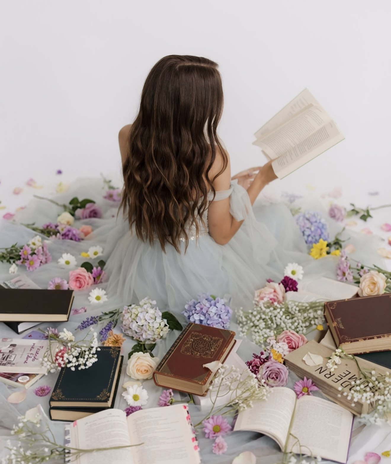 A girl in a blue tulle dress reads a book surrounded by colorful flowers and vintage books on a white background.