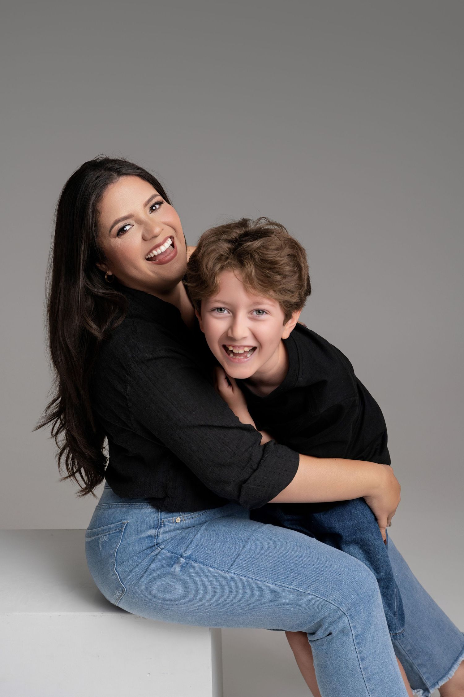 Mother and son in black tops hugging and smiling in studio portrait.