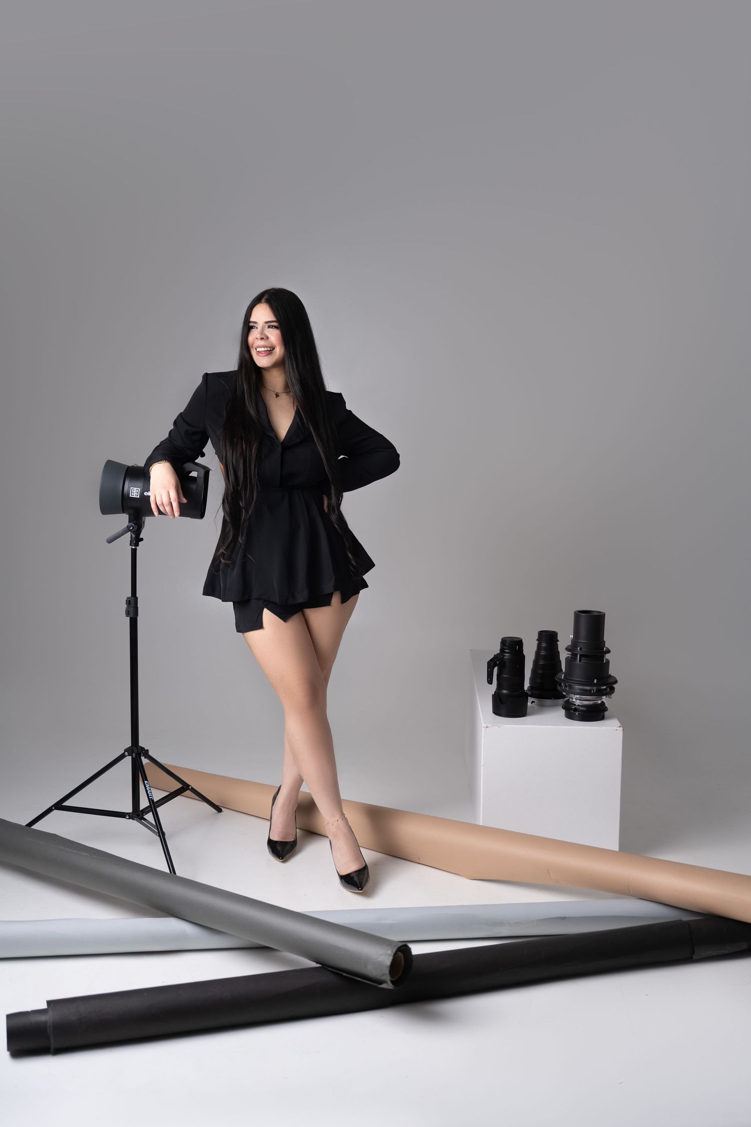 A series of minimalist fashion photographs showing a black dress against a gray backdrop with lighting equipment visible.