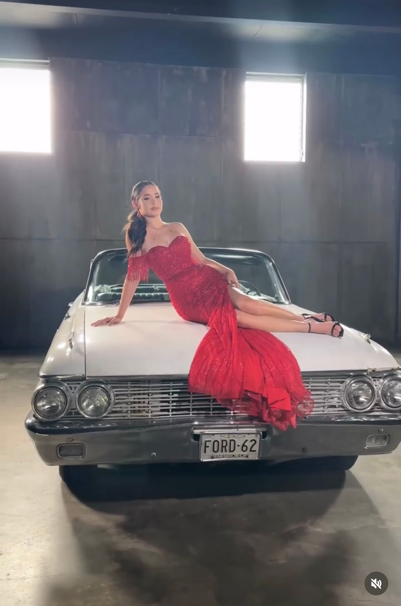 Woman in red lace gown poses on white 1962 Ford classic car in a dramatic indoor photoshoot setting.