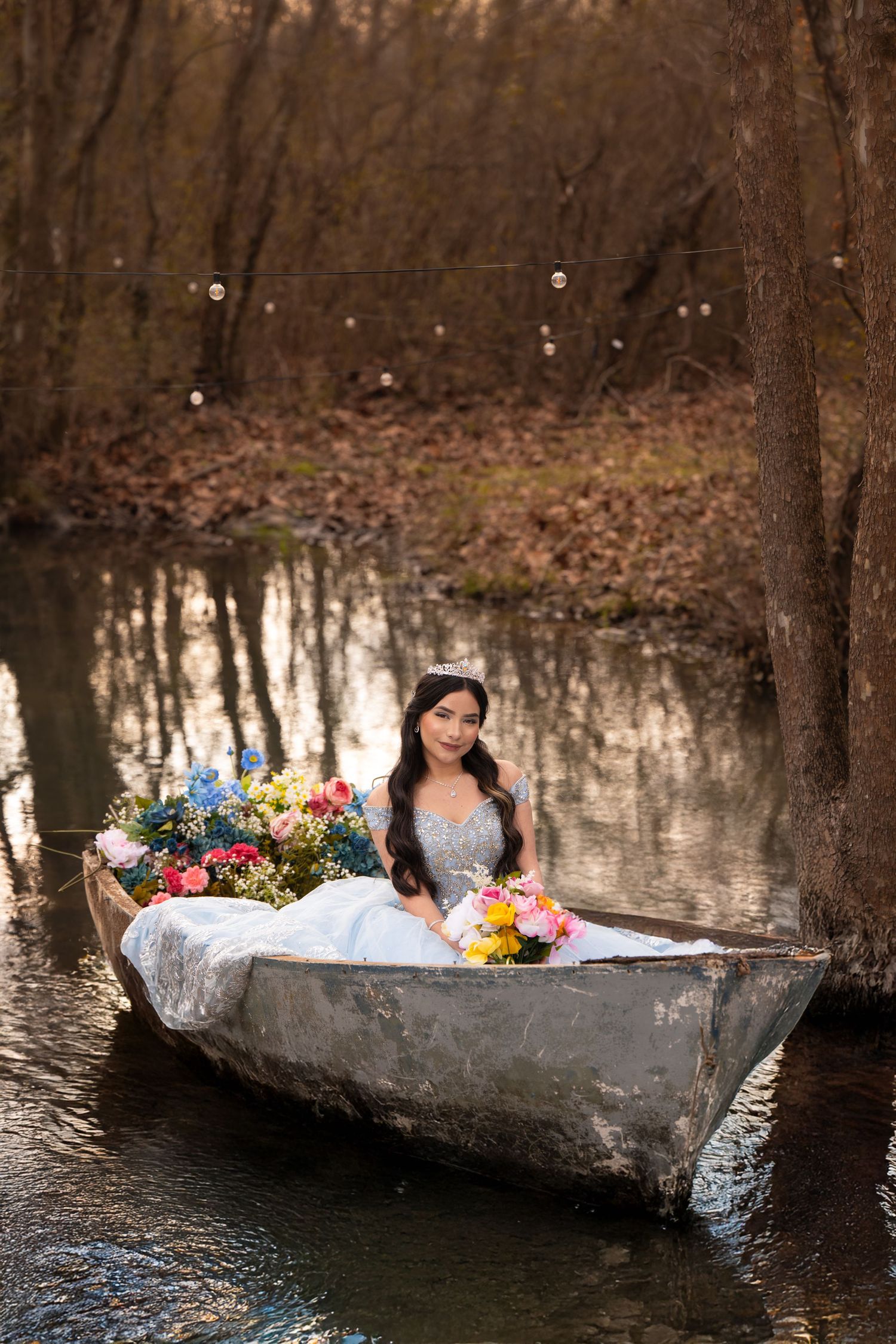Romantic scene with white-dressed figure in wooden boat surrounded by colorful flowers on calm water.