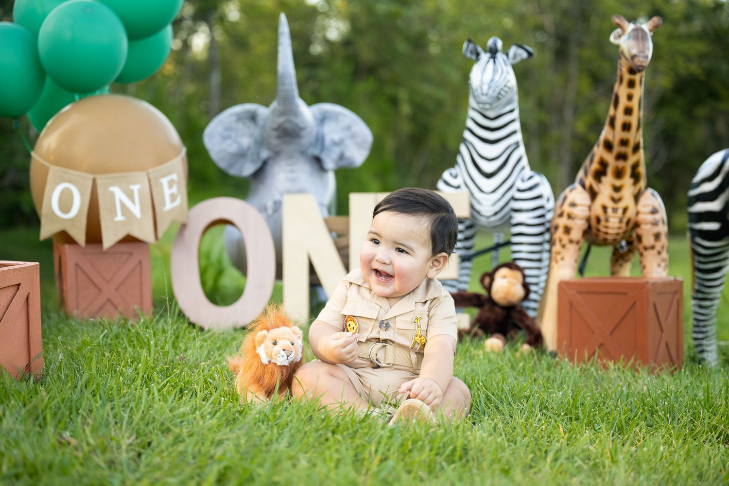 Safari-themed first birthday setup with stuffed animals and 'ONE' letter display.