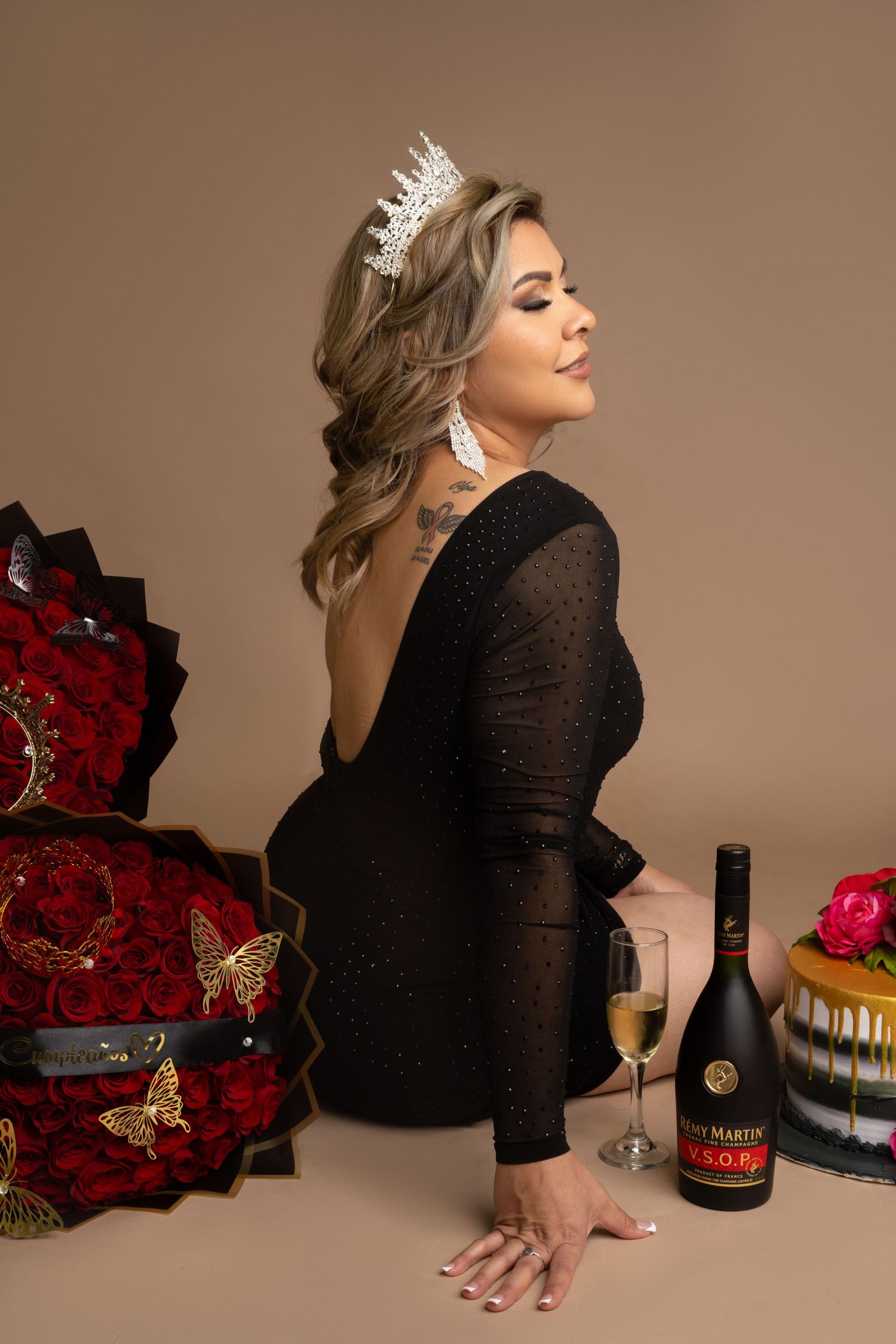 Glamorous celebration portrait featuring black dress, crown and red floral arrangements.