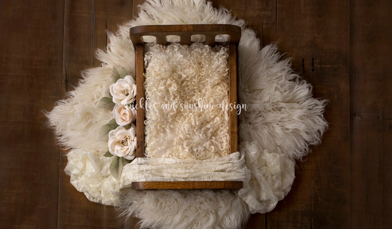 Rustic wooden box filled with cream lace fabric nestled on white fur backdrop with delicate pink roses.