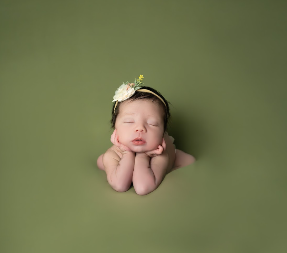 Peaceful newborn baby resting on olive green backdrop in minimalist photography style.