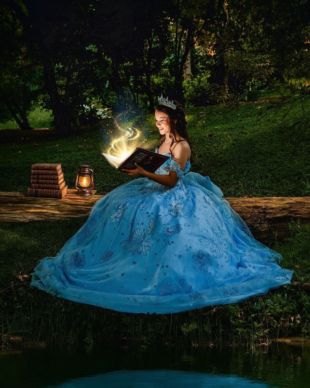 A young woman in a blue ball gown and crown reads a glowing magical book outdoors at night by a lantern.