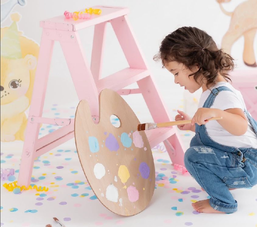 A child plays with colorful confetti and a large pink letter K on a white floor.