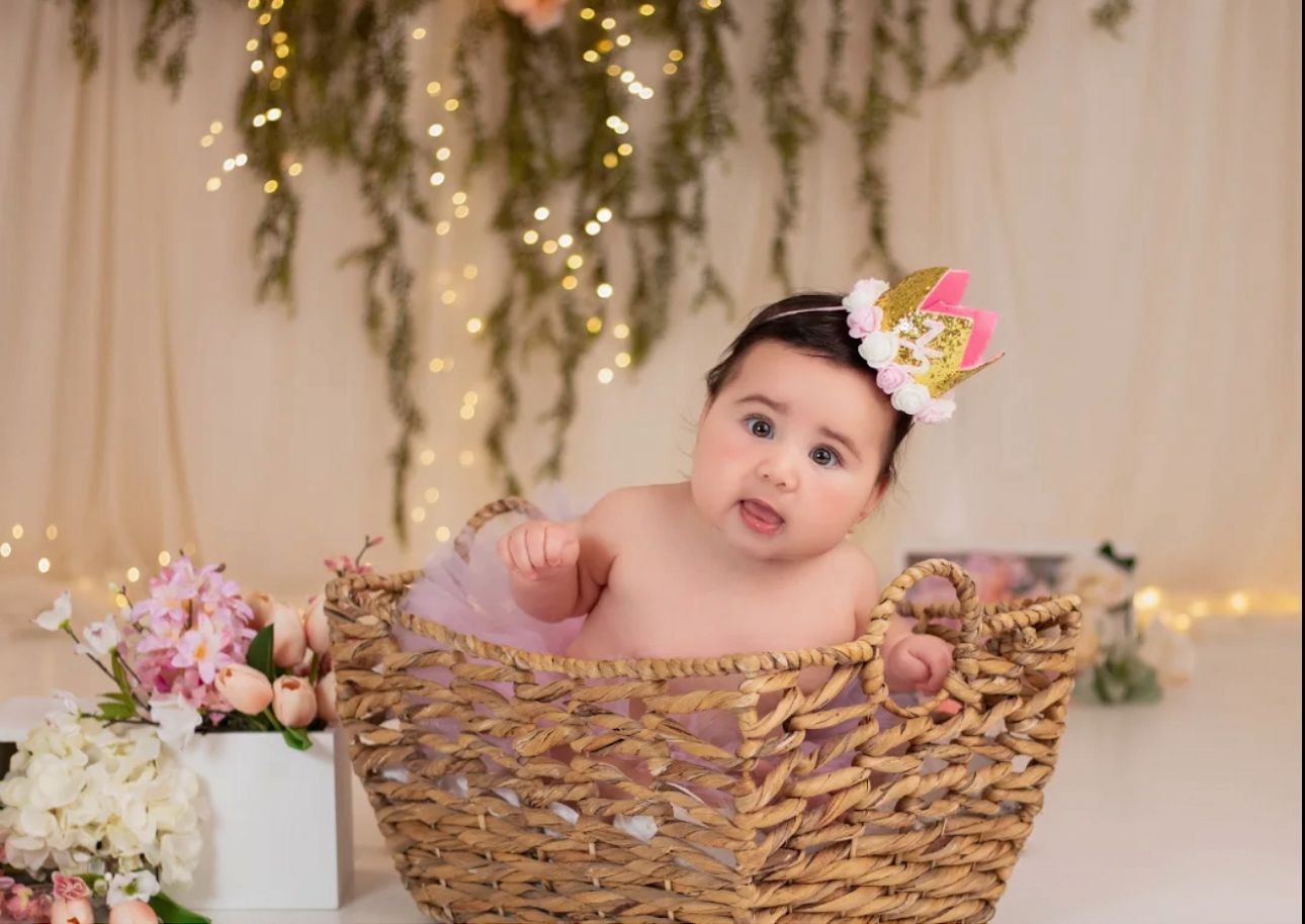 Baby photography setup in woven basket with floral decorations and twinkle lights.