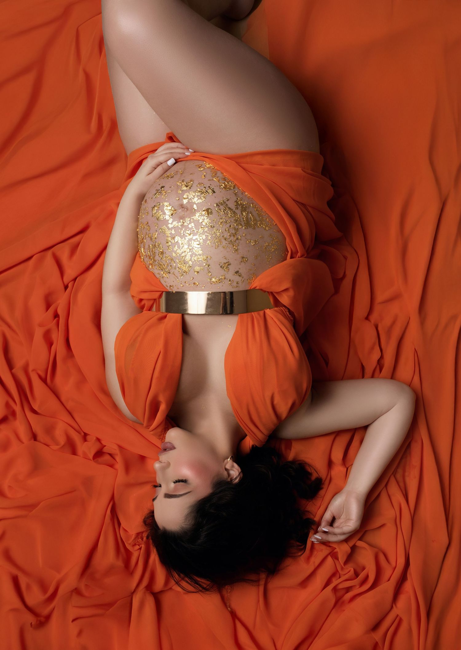 Artistic fashion photo with orange fabric backdrop and gold glitter bodice detail on an elegant dress.