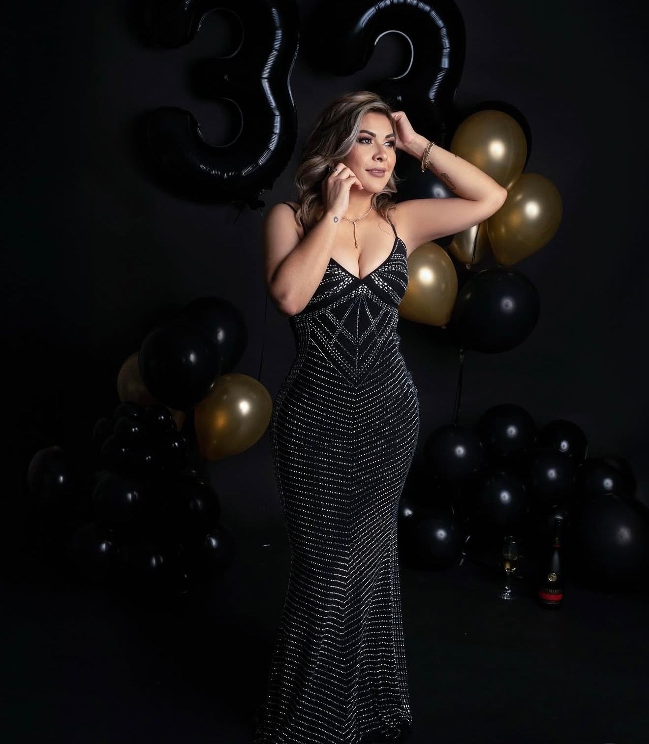 Woman in black sequin gown poses elegantly among black and gold balloons celebrating a 33rd birthday.