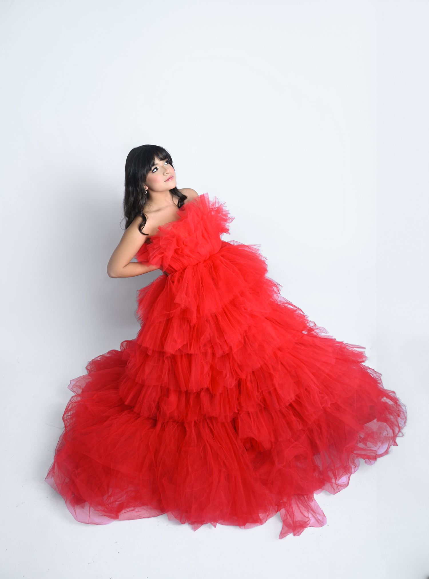 Woman in stunning red ruffled tulle ball gown posing gracefully against white background.