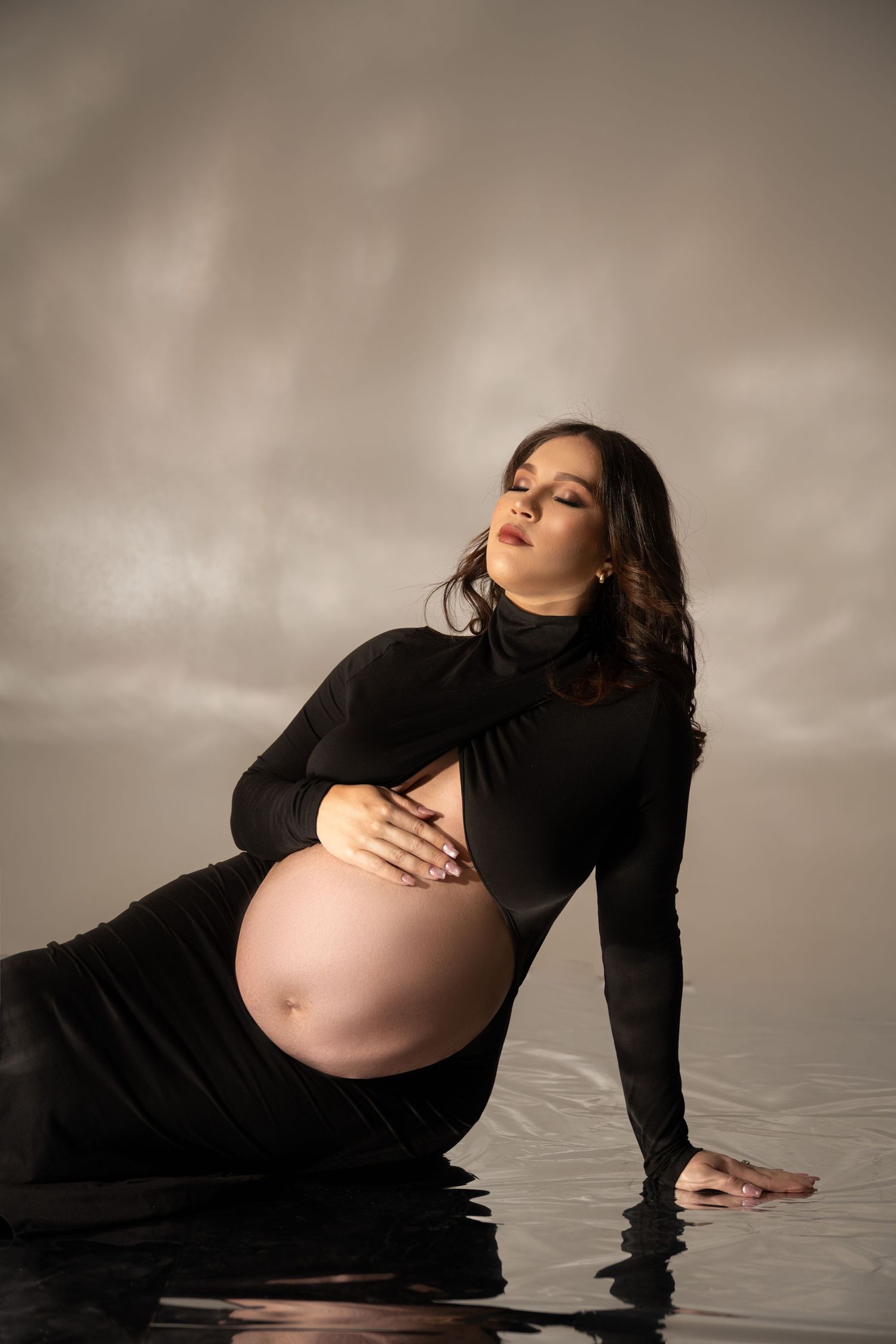 Serene maternity portrait in water wearing black dress with dramatic lighting.