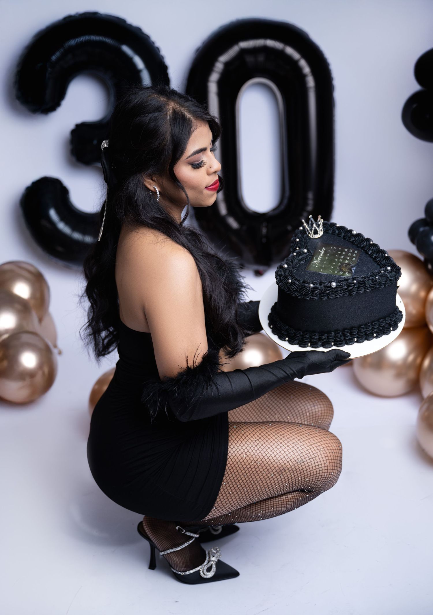 Glamorous birthday scene with black cake and metallic balloon decorations.