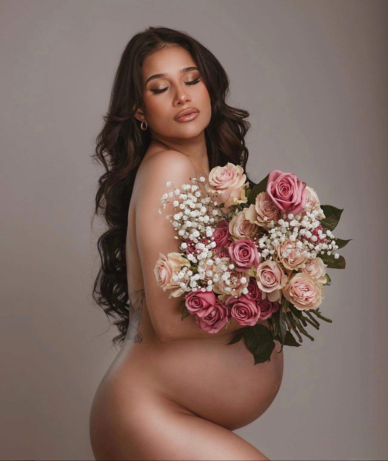Pregnant woman posing gracefully with a bouquet of pink and white roses in a studio maternity photo.