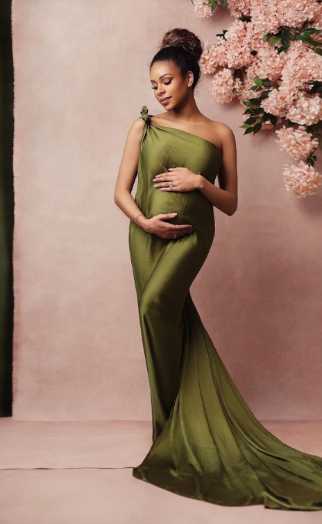 Maternity photoshoot in olive green flowing gown against pink backdrop with cherry blossoms.