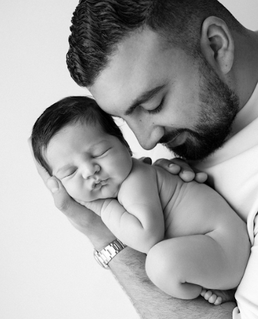 Black and white close-up photo showing tender moment between parent and sleeping baby in intimate portrait series.