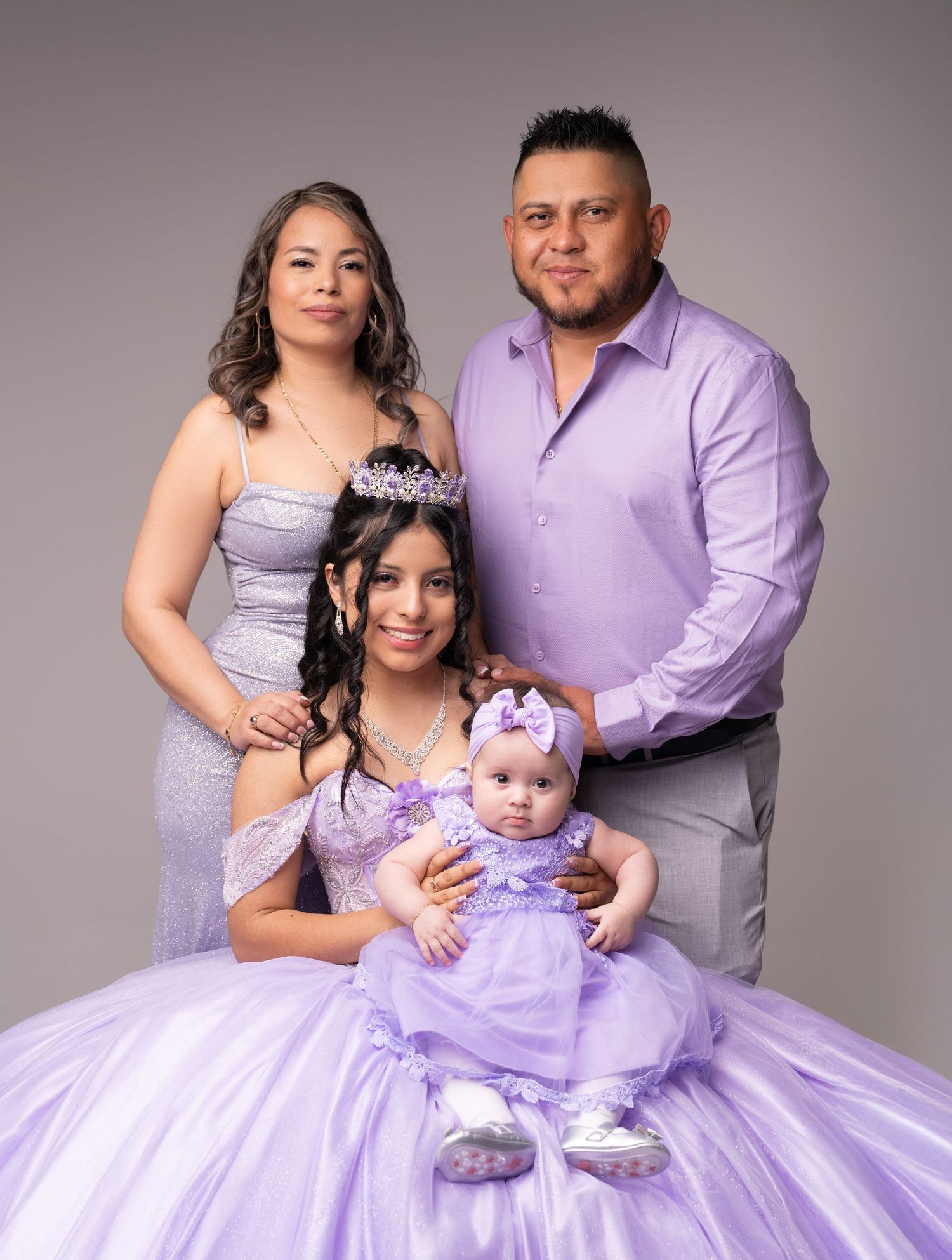 Family portrait in lavender outfits celebrating a quinceañera with parents, teen girl in gown, and baby.