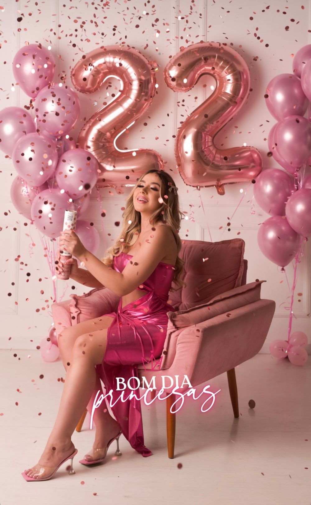 Woman in pink dress celebrating 22nd birthday with balloons, confetti, and a champagne popper in a pink-themed photoshoot.