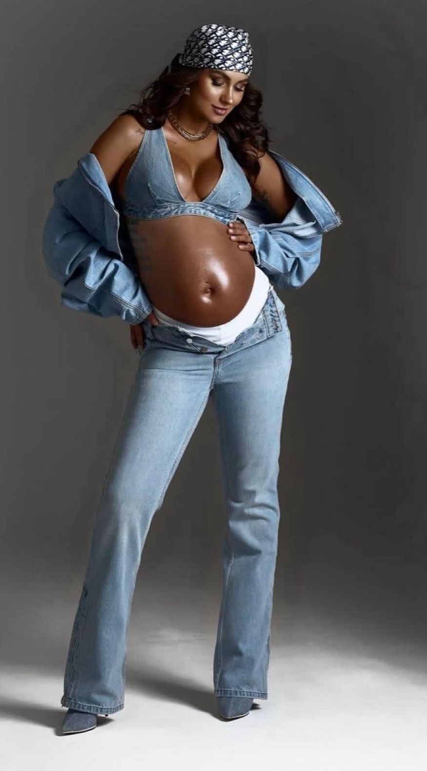 Pregnant woman in denim outfit and headscarf looking down at large baby bump.