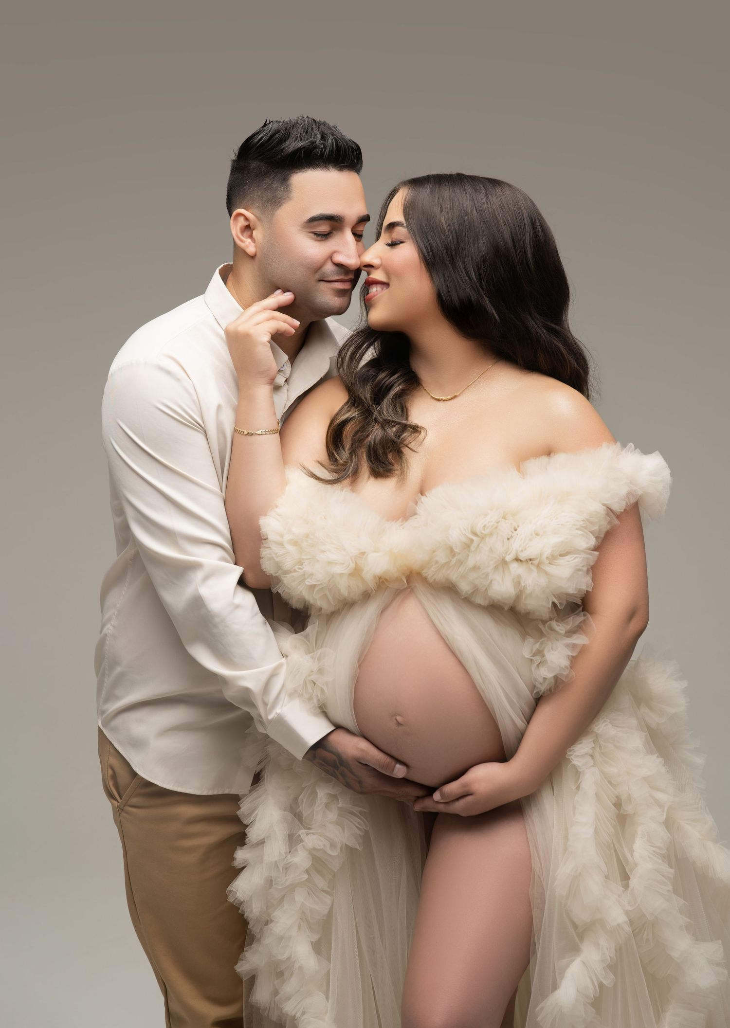 Intimate maternity photo featuring a couple embracing in cream and white tones against neutral background.