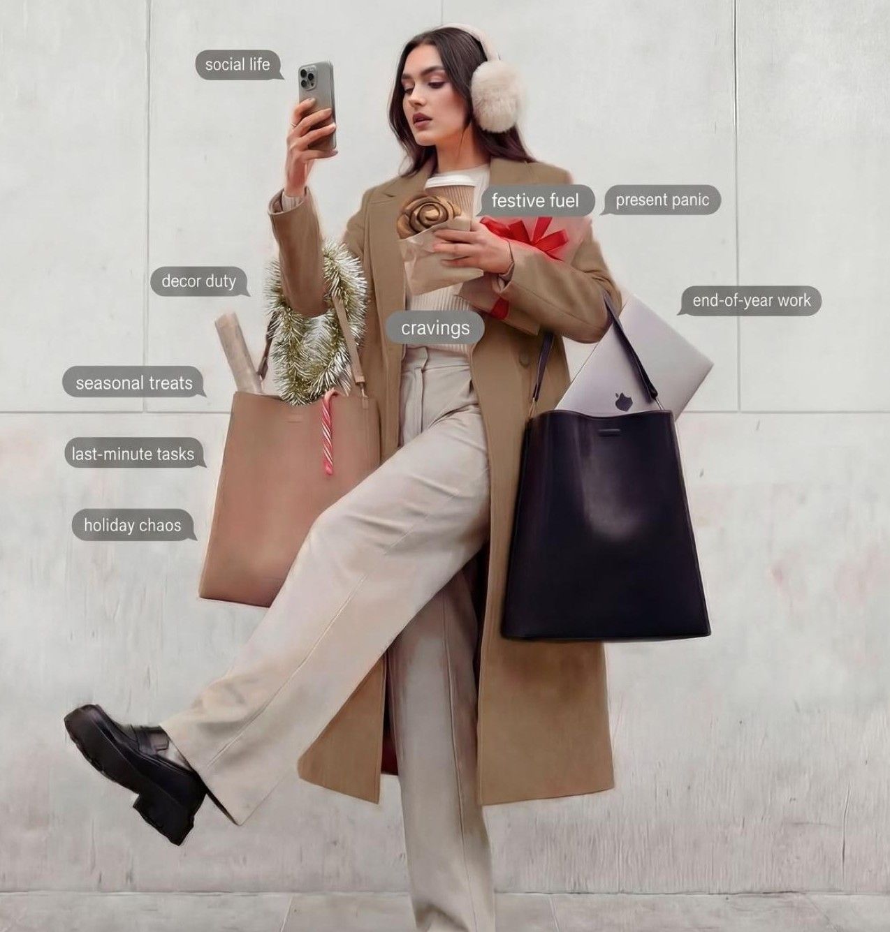 Stylish woman in beige coat and pink earmuffs juggling holiday tasks, bags, and coffee while checking her phone.