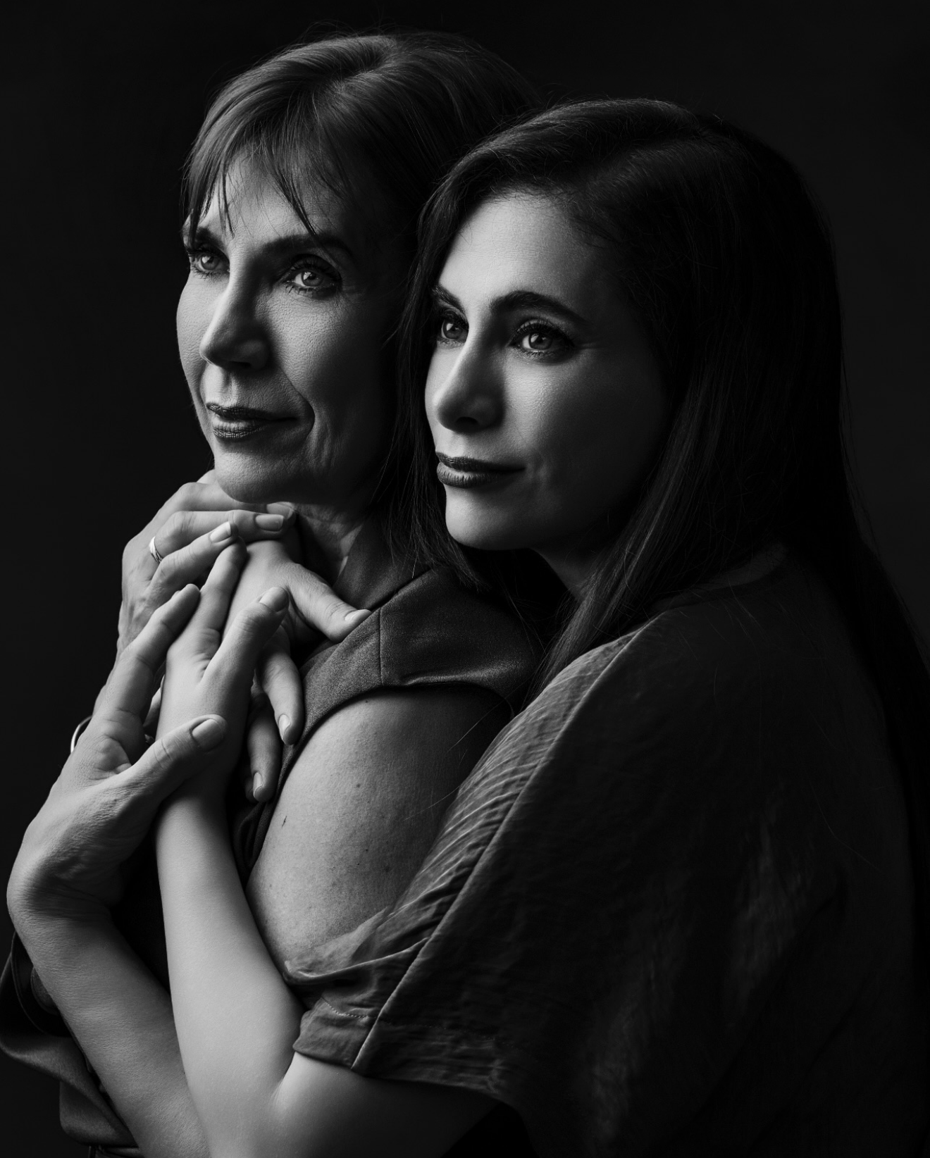 Black and white portrait of two women embracing, younger woman hugging older woman from behind in a tender pose.