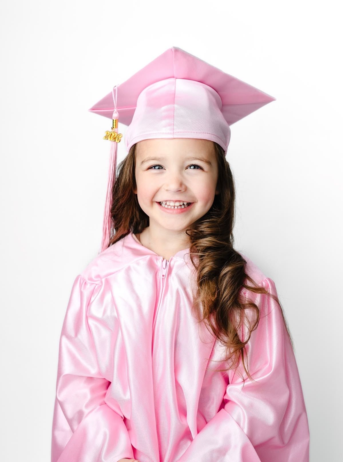 Smiling young girl wearing a pink graduation cap and gown, celebrating her preschool graduation.
