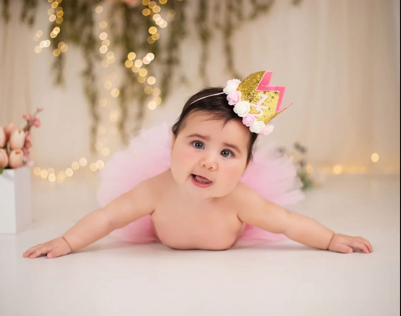 Baby milestone photo session with fairy lights and pink tulle in elegant setting.