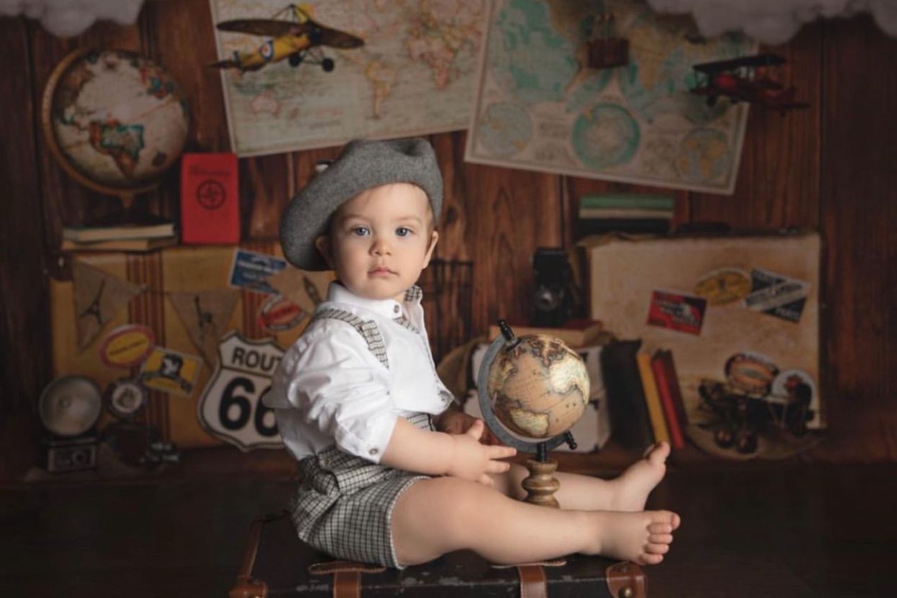 A vintage-themed photo setup with a globe, maps, and travel decor featuring a small child in retro attire.