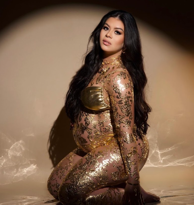 Artistic maternity photoshoot featuring gold glitter body paint and dramatic lighting against dark background.