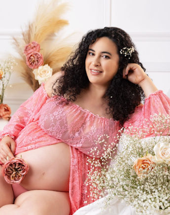A maternity photoshoot featuring soft pink lace lingerie with romantic floral and pampas grass decorative elements.