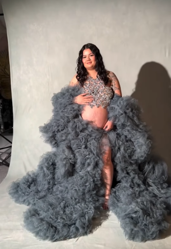 A maternity photo featuring a dramatic grey tulle gown and sparkly top against a white studio backdrop.