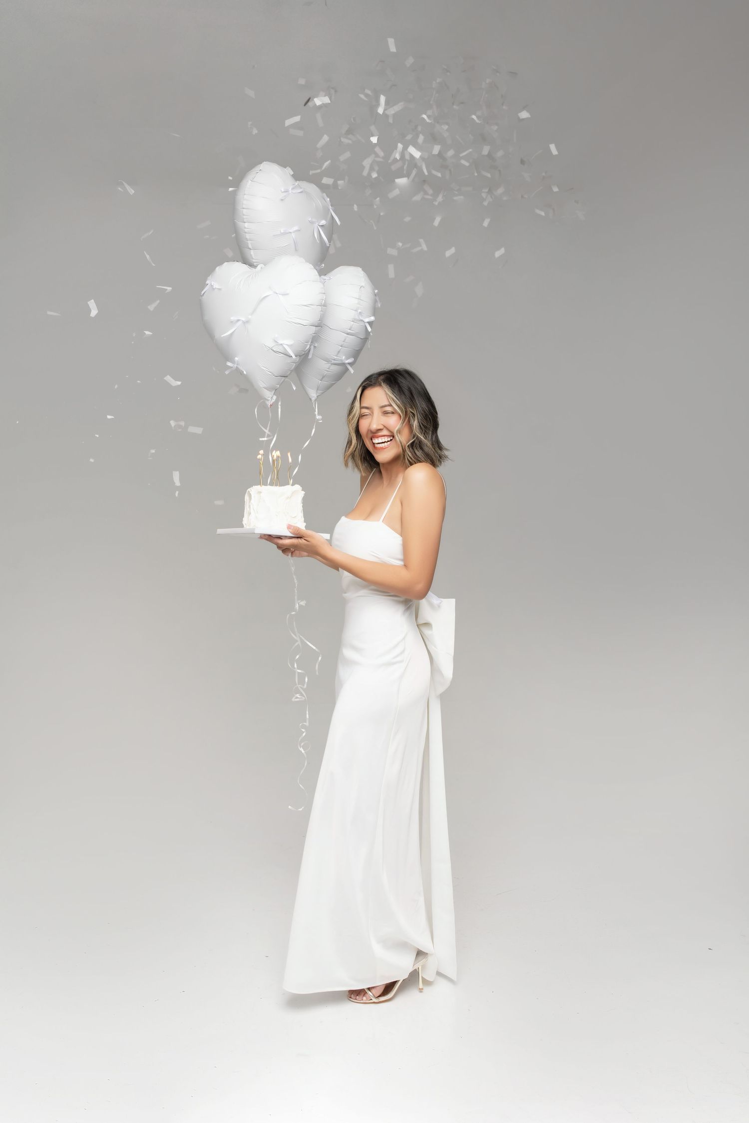 A series of four photos shows someone in a white dress holding a white box against a light gray background.