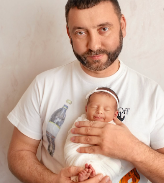 A sleeping newborn baby wrapped in white swaddling cloth being cradled in gentle arms.