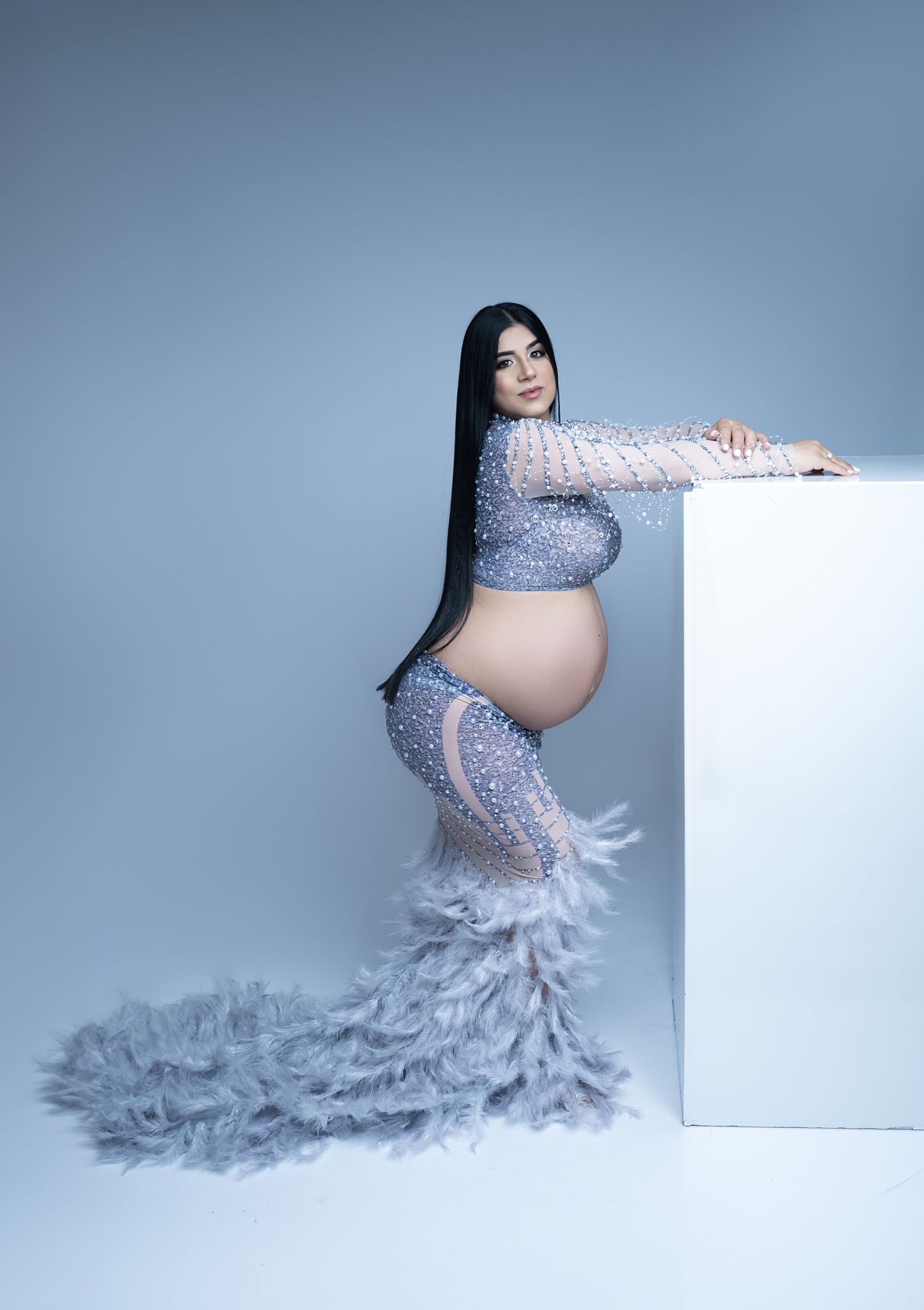 Glamorous maternity portrait in silver sequined gown with feather train.