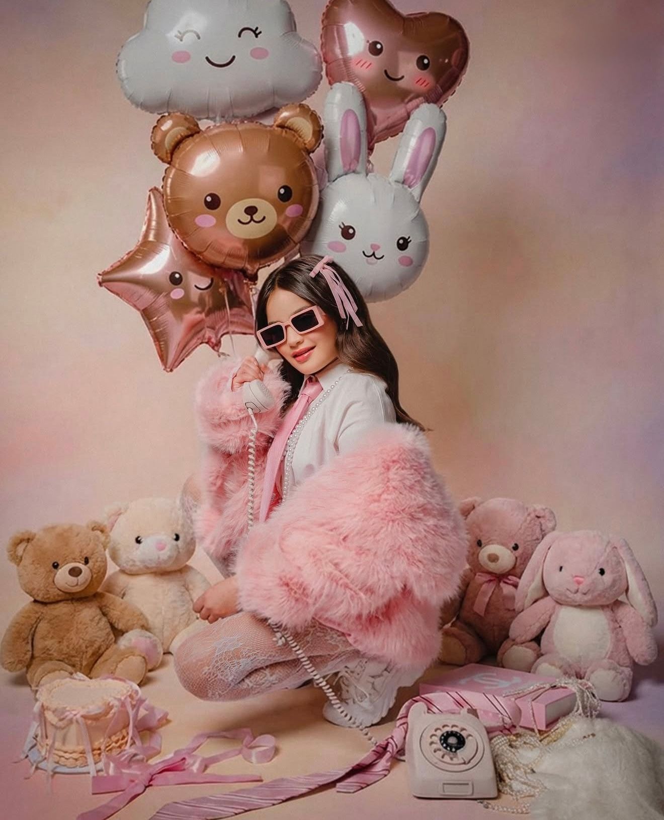 Young woman in pink fluffy coat poses with teddy bears, bunny plush toys, and colorful balloons in a dreamy pink setting.