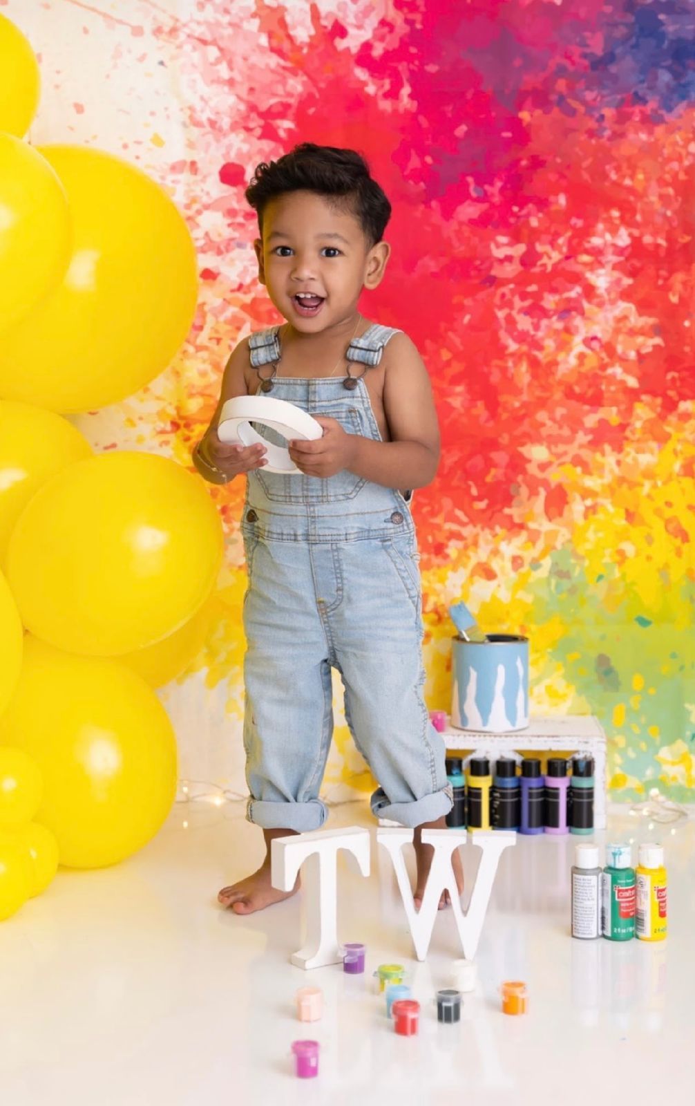 Vibrant art setup with yellow balloons against a colorful paint-splattered backdrop with paint jars.