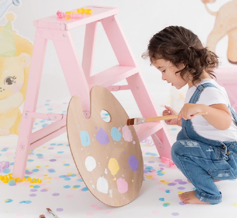 Colorful first birthday photo session with pastel pink decorations, cake smash setup, and scattered confetti on white backdrop.