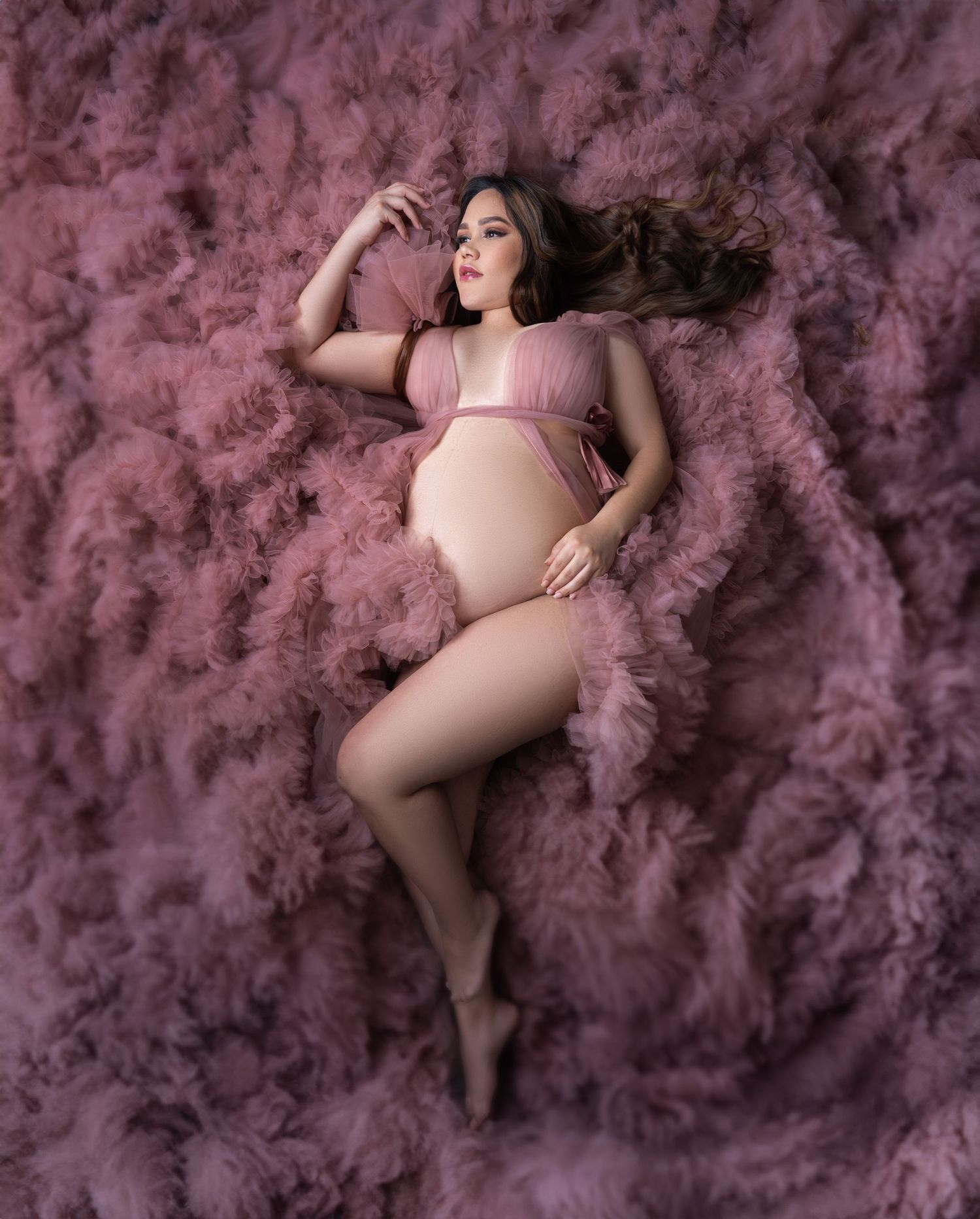 A dreamy maternity photo with pink tulle fabric creating a cloud-like effect.