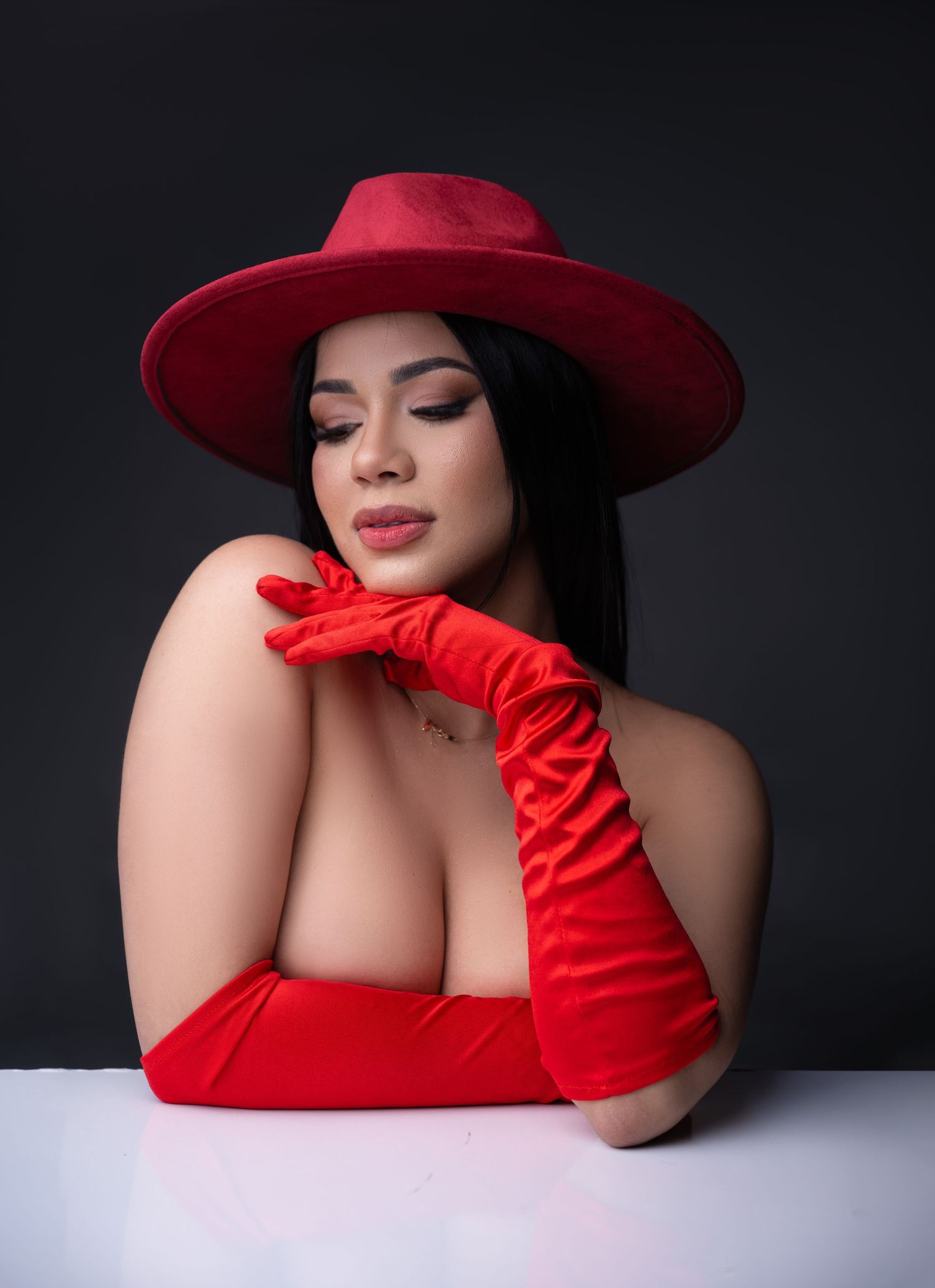 Woman in red wide-brim hat and long red velvet gloves posing elegantly against a dark background.