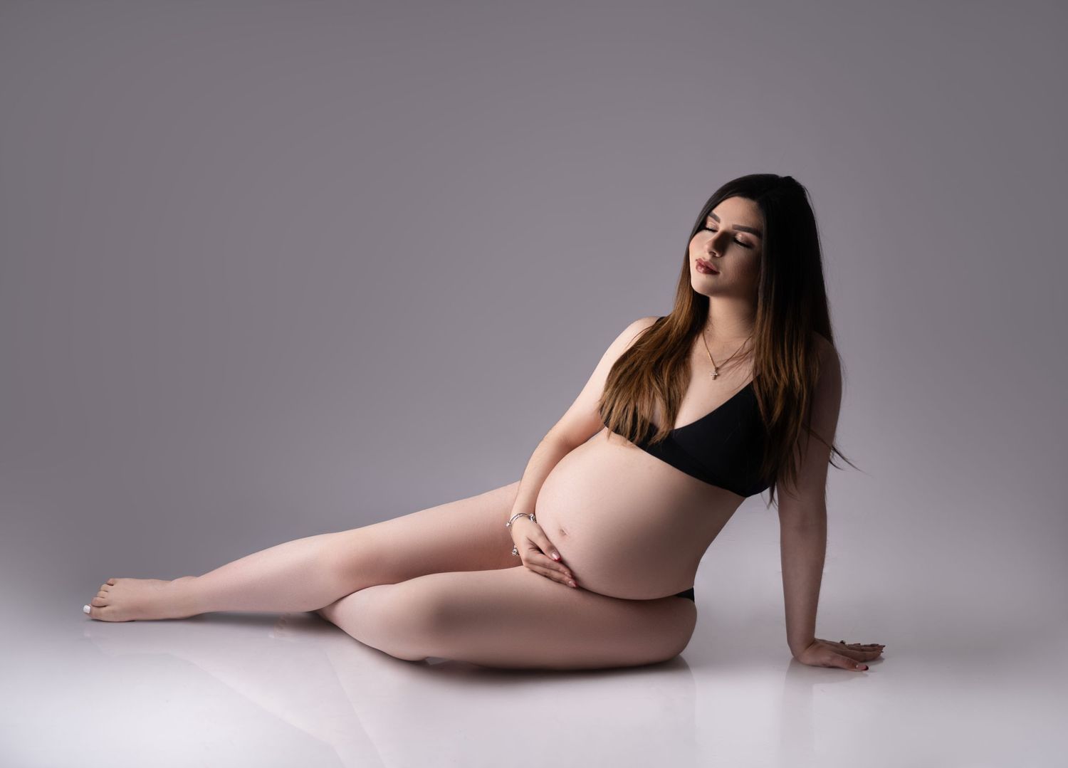 Elegant maternity pose with subject in black attire laying on studio floor.