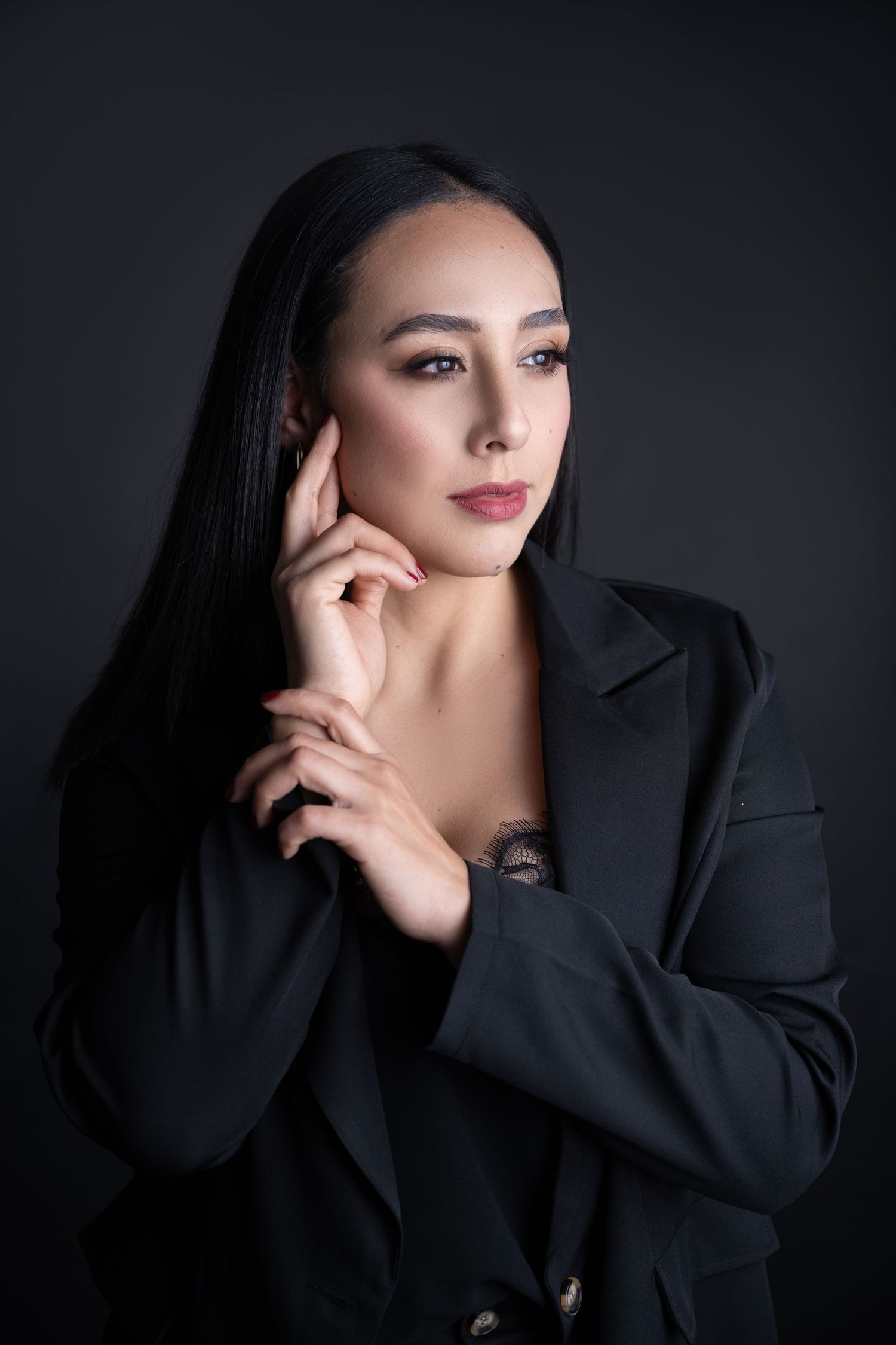 Elegant portrait of woman in black blazer against dark background with dramatic lighting.